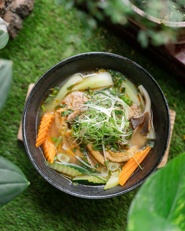 Vegane Nudelsuppe mit Pak Choi, Karotten und Frühlingszwiebeln in einer dunklen Schale